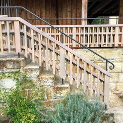 Ein robustes Holzgeländer, gefertigt in traditioneller Zimmerei, entlang einer alten Steintreppe, die zu einem hölzernen Gebäude führt.