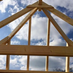 Detailansicht eines Dachstuhls im Bau, gezeigt in feiner Zimmerei, mit blauem Himmel und Wolken im Hintergrund.