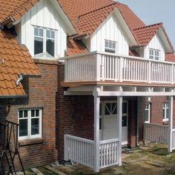 Detaillierte Ansicht eines neu errichteten Holzbalkons als Beispiel für die Arbeit einer Zimmerei, integriert in ein Backsteinhaus mit Ziegeldach.