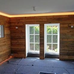 Zimmer mit Wänden aus Holzplanken, ein Beispiel für die präzise Arbeit einer Zimmerei, mit großen Fenstern, die Gartenblick bieten.