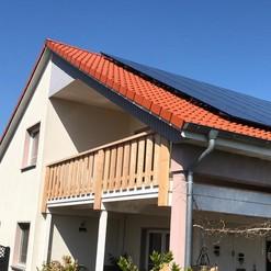 Modernes Haus mit einem oberen Holzbalkon, hervorgehoben durch die feine Arbeit einer Zimmerei, umgeben von einem gepflegten Garten.
