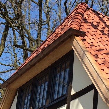 Detailaufnahme des Giebels eines Fachwerkhauses mit Ziegeldach und Holzfenstern.