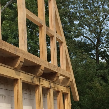 Aufbau eines Fachwerkbaus mit sichtbaren hölzernen Strukturen und Balken vor einem Hintergrund aus Bäumen.