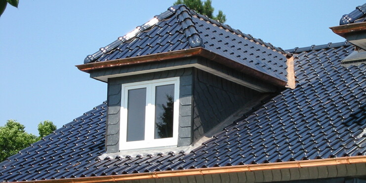 Nahaufnahme einer modernen Dacheindeckung mit glänzenden blauen Dachziegeln, Kupferdetails und einer kleinen Gaube.