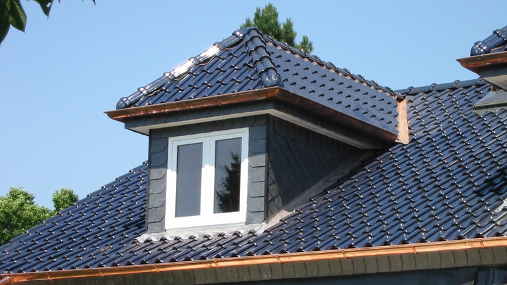 Nahaufnahme einer modernen Dacheindeckung mit glänzenden blauen Dachziegeln, Kupferdetails und einer kleinen Gaube.