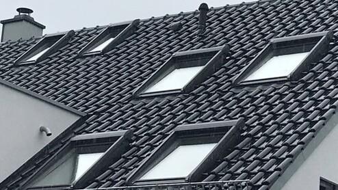 Dachsanierung Blick auf ein Dach mit schwarzen Dachziegeln und 6 Velux-Fenstern