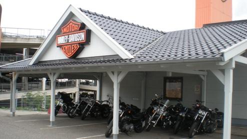 Überdachter Carport mit Harley-Davidson Logo, bietet Schutz für mehrere Motorräder unter einem grauen Ziegeldach.