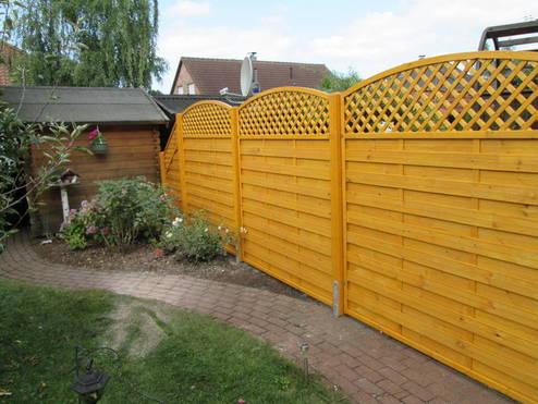 Stilvoller Holzzaun in leuchtendem Gelb mit Latten- und Gitterstruktur, umgesetzt durch professionellen Zaunbau, umgibt einen gepflegten Garten.