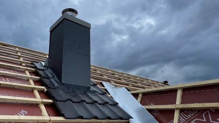 Installation eines Schornsteins auf einem Dach Neuer Schornstein auf einem noch nicht fertiggestellten Dach, umgeben von wasserdichter Folie, unter dramatischem Himmel – ein Beispiel für modernen Schornsteinbau.