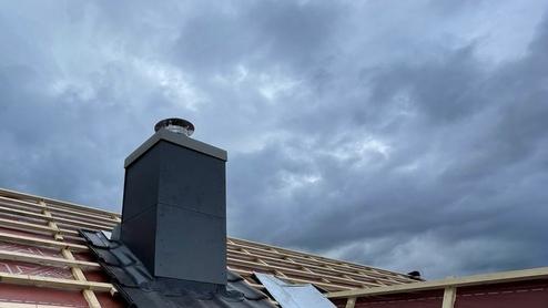 Neuer Schornstein auf einem noch nicht fertiggestellten Dach, umgeben von wasserdichter Folie, unter dramatischem Himmel – ein Beispiel für modernen Schornsteinbau.