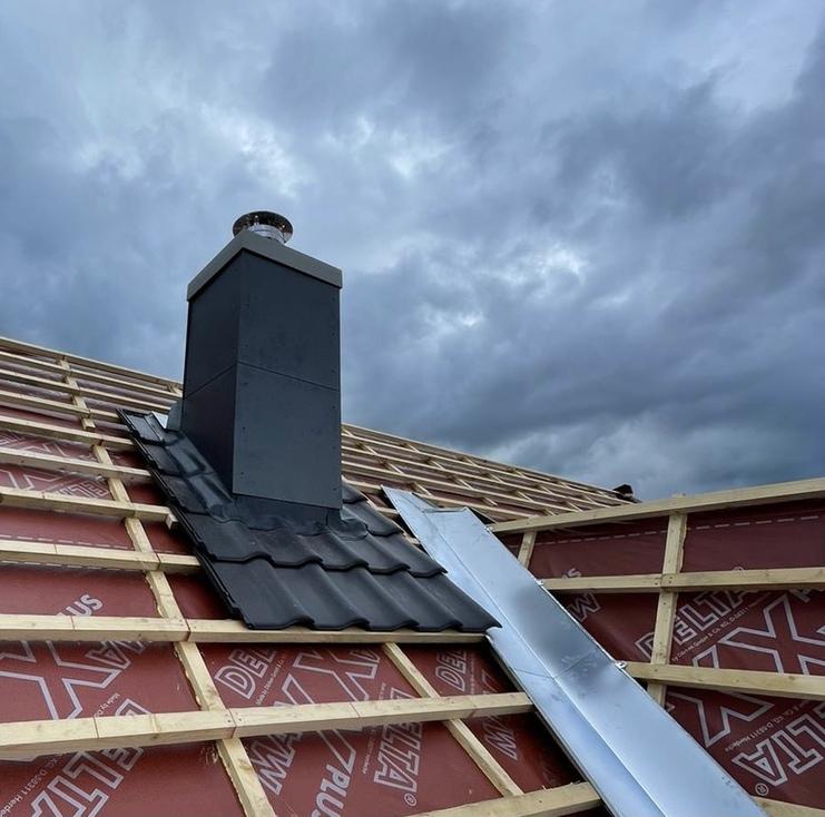 Installation eines Schornsteins auf einem Dach Neuer Schornstein auf einem noch nicht fertiggestellten Dach, umgeben von wasserdichter Folie, unter dramatischem Himmel – ein Beispiel für modernen Schornsteinbau.